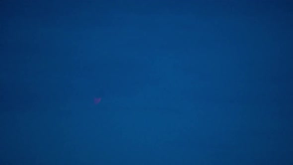 Red colored blood moon during lunar eclipse moving behind clouds at dusk alt