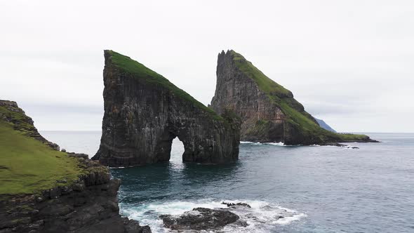 Aerial View of the Rocky Drangarnir Sea Stack in the Faroe Islands and the Skarosafossur Waterfall alt