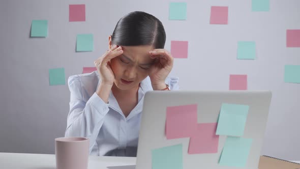 Asian woman working on a laptop has headache sitting