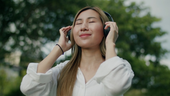 Asian female enjoying the breeze outdoors and having fun wearing headphones listening to music.