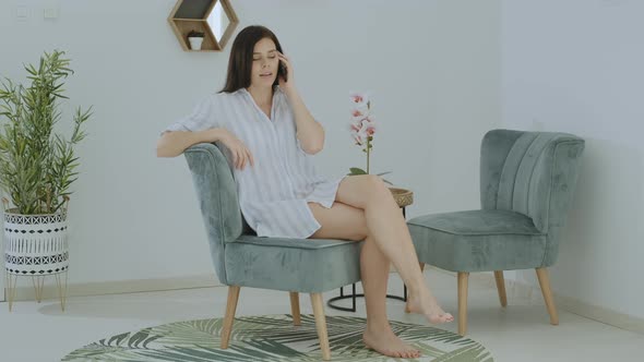 Pretty woman in casual home clothes calling and waiting answer using phone in apartment. alt