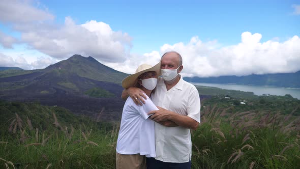 Portrait of Middleaged Couple in Face Masks Hugging in Front of Mountains and Ocean alt