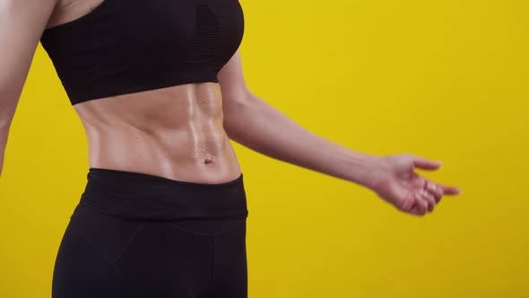 Woman in a sports uniform shows on muscular belly with hands in the studio, close-up. alt