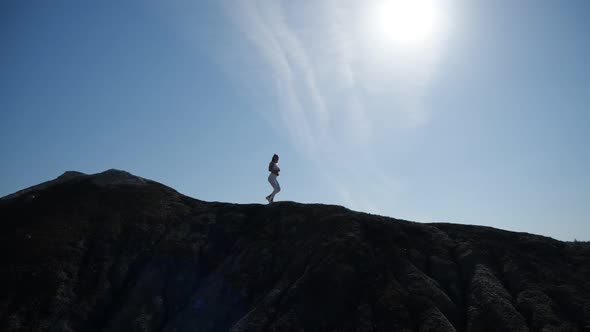 The Silhouette of a Girl Running High on the Edge of a Hill.