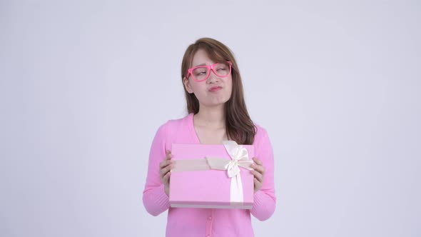 Young Happy Asian Nerd Woman Thinking While Holding Gift Box alt