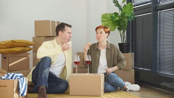 Married Couple Eat Sandwich Drinking Red Wine Celebrating Relocation And Moving Into New House