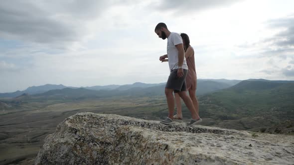 Young Couple in Love Rises To the Edge of a Cliff Against the Backdrop Mountains
