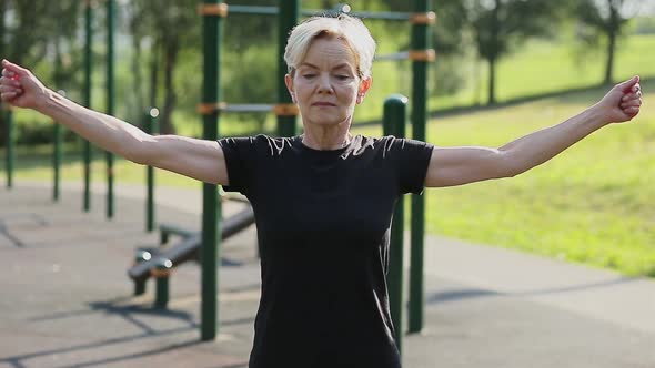 An Elderly Woman Does a Warmup in the Park on the Playground