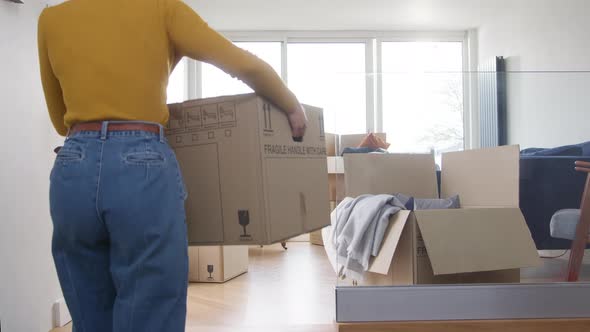 Young Woman Carrying Moving Box Into Lounge Of New Home And Looking Around