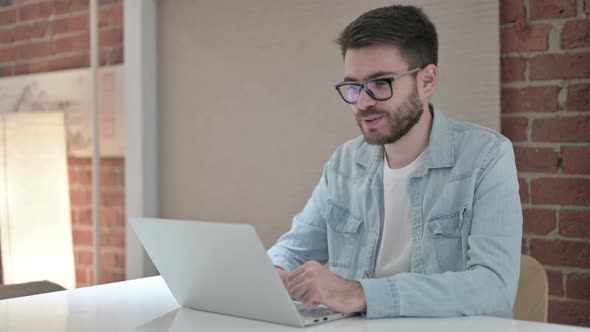 Cheerful Young Male Designer Doing Video Chat on Laptop alt