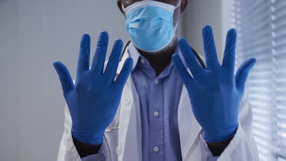 Midsection of mixed race male doctor wearing face mask and surgical gloves alt