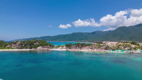 Drone flying over the crystal clear blue waters of Binh Tien Beach surrounded by green cliffs in Vie alt