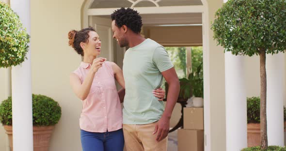 Happy biracial couple holding keys to new house and embracing with joy alt