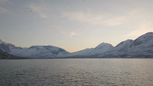 Aerial over open arctic ocean, view of snowy mountains on mainland alt