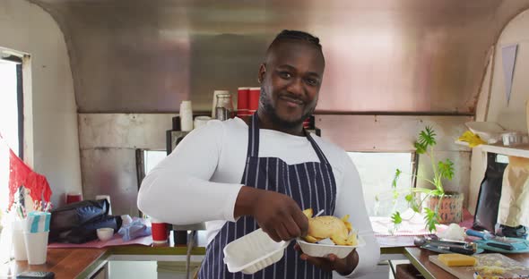 Smiling african american male business owner holding takeaway meal in food truck alt