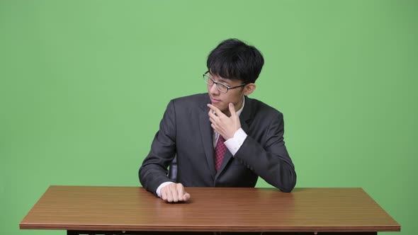 Young Asian Businessman Bored and Tapping Fingers on Table alt