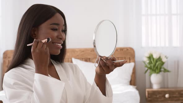 Black Woman Making Makeup Using Cosmetic Brush Sitting In Bedroom alt