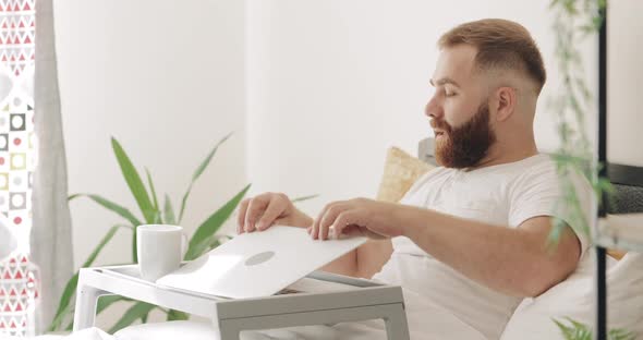 Side View of Adult Male Freelancer Finishing Work and Drinking Hot Coffee. Handsome Bearded Guy in alt