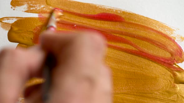 Drawing with a Paintbrush on White Paper with Bright Golden Acrylic Paint Close Up alt