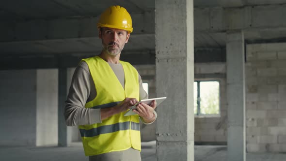 Caucasian engineer walking and browsing digital tablet on construction site. alt