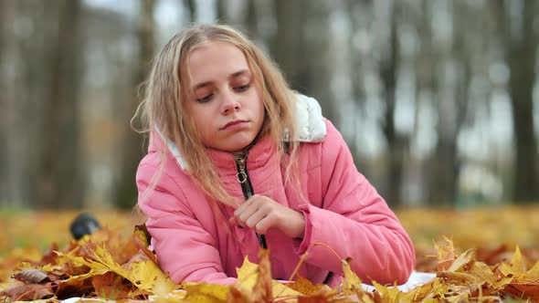 Teenage Girl Crying in the Autumn Foliage in the Park. alt