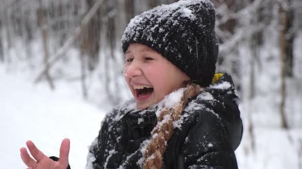 Snow falls on the face of a laughing teenage girl in winter clothes, in a park.