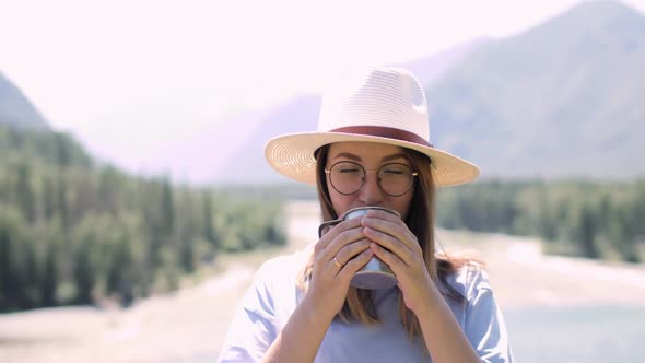 Young Woman in Hat Drinking a Tea in Mountains at Summer Sunny Day, Front View.