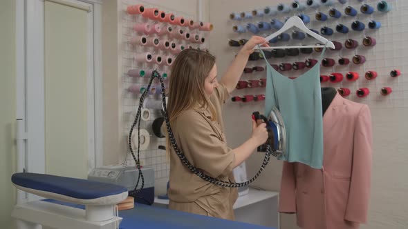 A fashion tailor designer at work hovering clothes with an iron and steam in a sewing workshop alt
