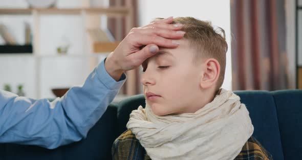Tired Upset Sick Boy with Pain in Throat Sitting on the Couch when Mother Checking His Temperature alt