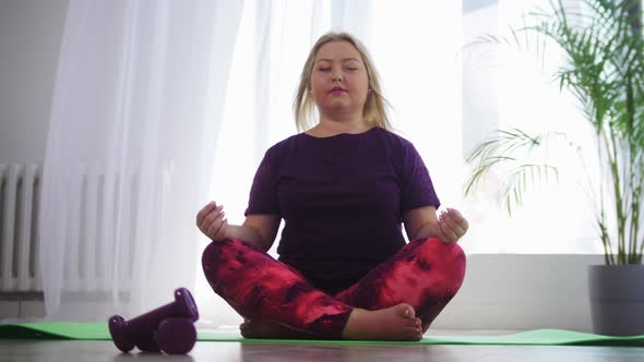 Yoga Indoors  Blonde Overweight Woman Meditating on Yoga Mat in White Modern Studio alt