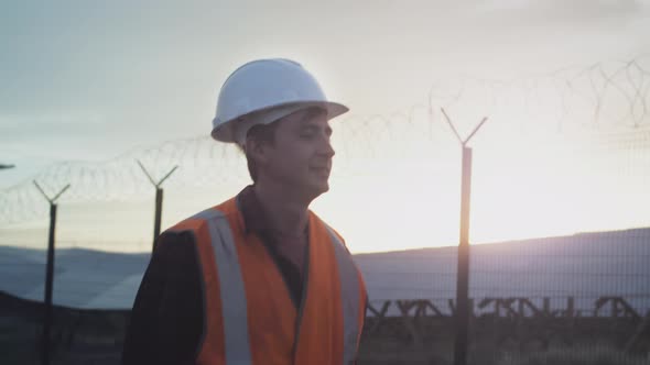 A Male Professional Worker Engineer Walks Next to a Solar Panel Farm alt
