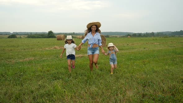 Mum Holding Hands With Kids and Running on the Field With Haystacks