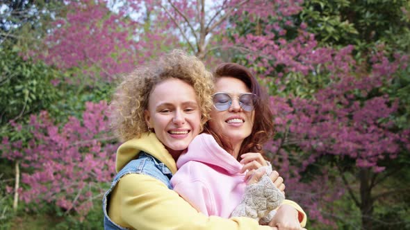 Homosexual Lesbian Couple Hugging in a Sakura Garden and Looks in To the Camera alt