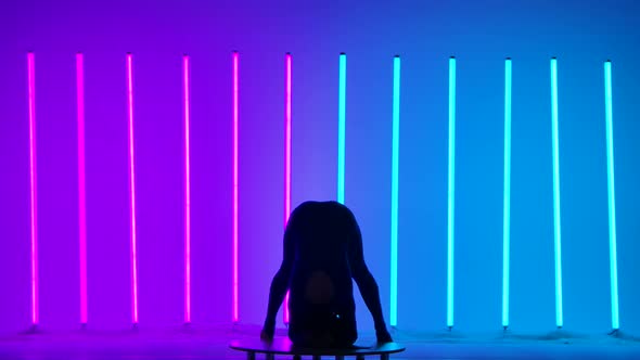 Silhouette of a Gymnast Against the Background of Pink and Blue Neon Lamps alt