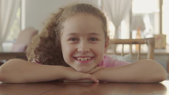 Portrait of a Happy Little Girl Smiling Child Looking at the Camera Sitting at the Table in a Cafe alt