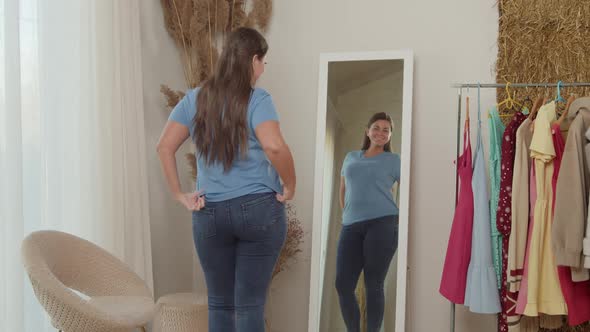 Cheerful Plump Woman in Jeans Admiring Reflection in Mirror Indoors alt