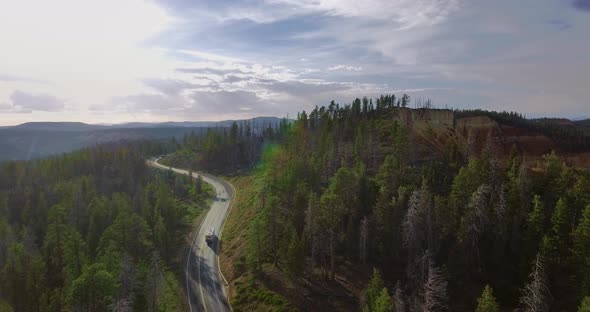 Drone moves behind a white caravan along a highway and green pines  (Zion National Park) alt