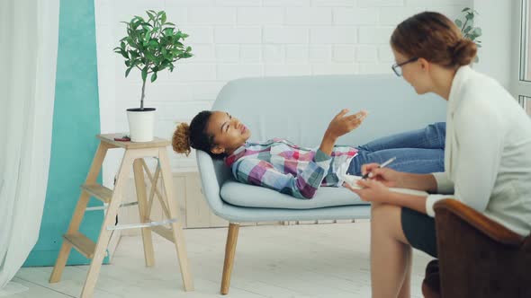 African American Teenager Is Talking To Psychologist Lying on Couch and Smiling alt