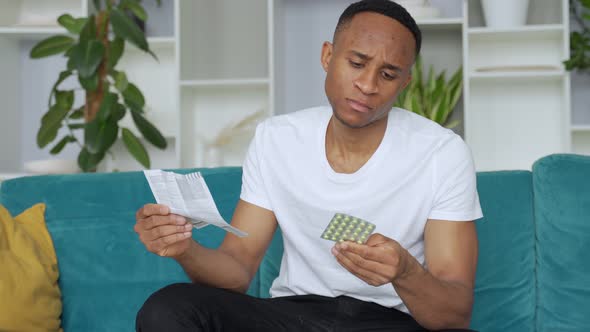 Black Man Alone Sitting on Sofa Sick Reading Instructions How To Take Pills Concentrated alt