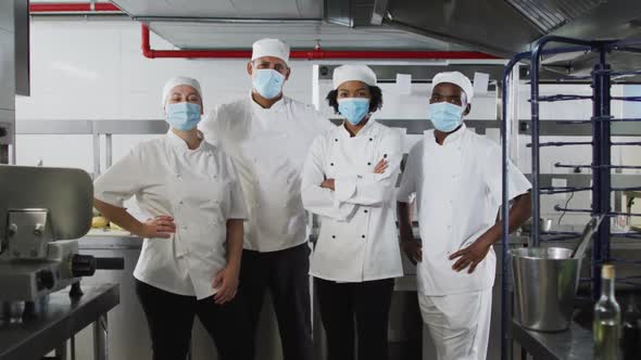 Portrait of diverse group of chefs wearing face masks standing in restaurant kitchen alt