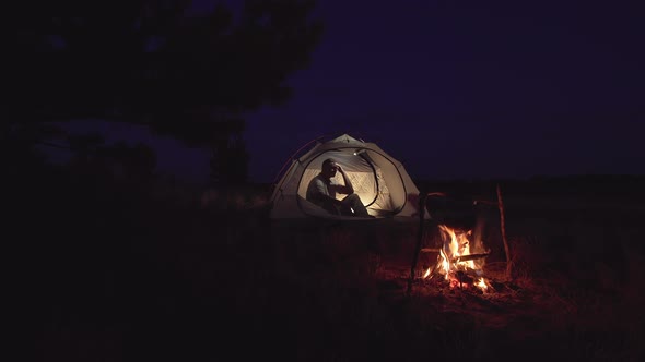 A Man Rests in a Tent Near a Fire alt