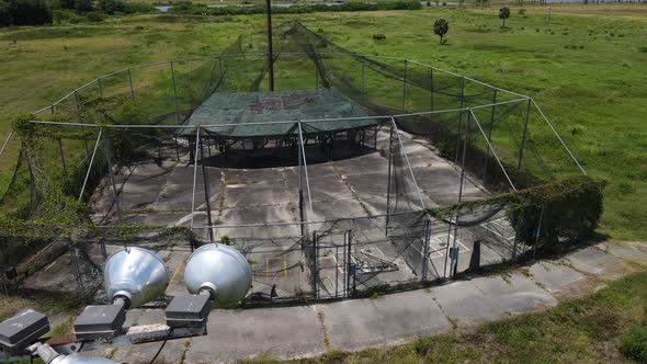 aerial of an abandoned amusement batting practice cage, dramatic flight by old lighting post alt