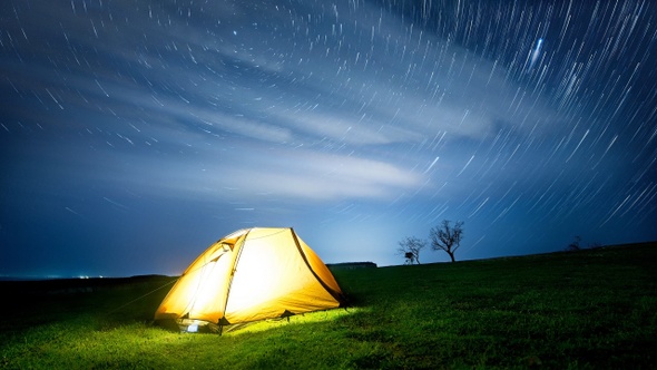 Time-lapse. Glowing camping tent in the night mountains under a star trails.