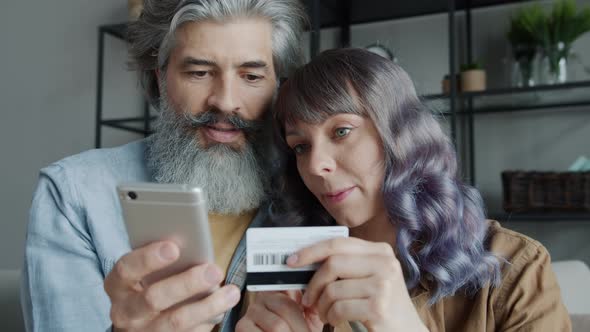 Mature Man and Young Woman Making Online Payment Using Smartphone and Credit Card at Home alt