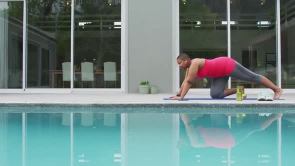 Happy african american plus size woman practicing yoga, stretching next to swimming pool in garden alt