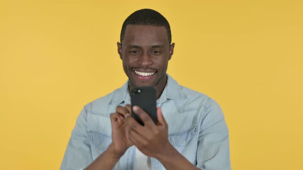 Young African Man Using Smartphone, Yellow Background  alt