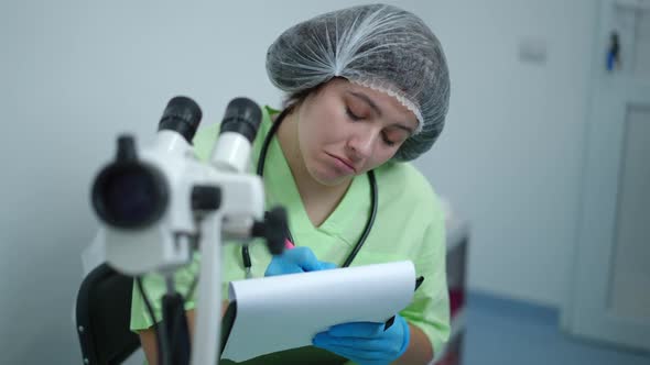 Concentrated Expert Obstetrician Using Gynecological Colposcope Writing with Pen Thinking alt