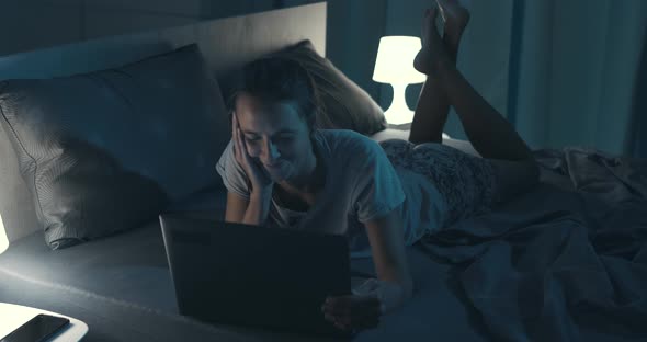 Woman lying in bed and connecting with her laptop late at night, she can't sleep