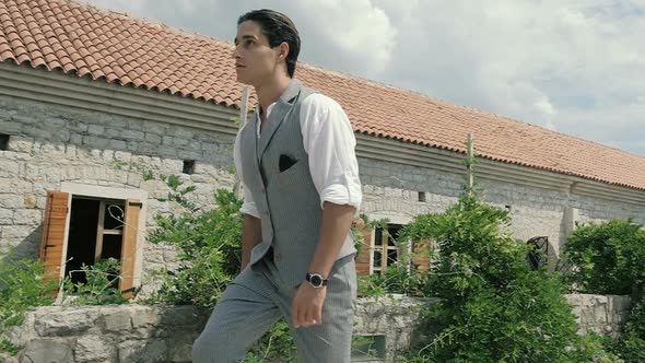 Attractive young fashion man in a suit walks around the old town along the plants. Slow motion alt