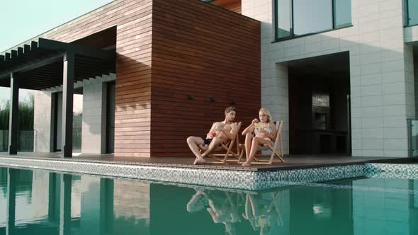 Beautiful Couple Drinking Cocktails Outside. Happy Couple Enjoying Sunbathing alt